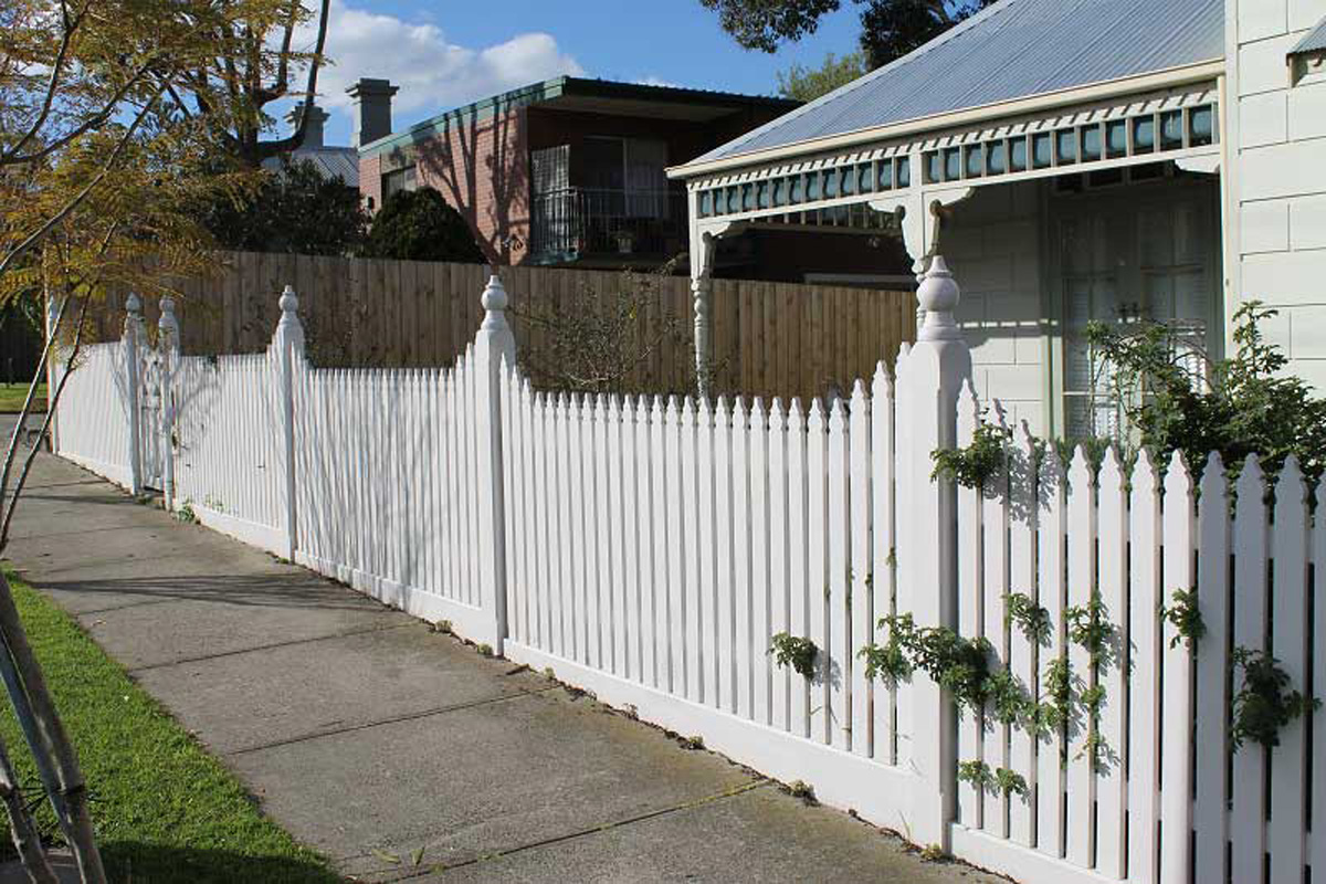 Newly built white traditional picket fence in front of colonial house.